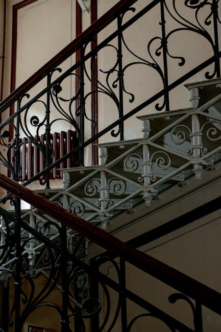 The image shows the exterior of a Victorian terraced house with a black front door, white decorative columns, and a bay window to the right of the entrance. The entrance is accessed via a small set of white steps with black metal railings on one side, leading up to the door which has a brass letterbox and door handle. In front of the house, a narrow paved pavement is visible, and there is a short white wall with a black wrought iron fence on top, separating the property from the sidewalk. The building's façade is made of brick with white painted trim around the windows and door. The overall scene depicts a typical London residential property, consistent with house relocation and furniture transport processes often handled by companies like Man with Van Primrose Hill during packing and moving services.